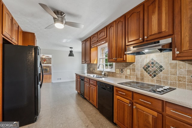 kitchen featuring under cabinet range hood, a sink, light countertops, brown cabinets, and black appliances