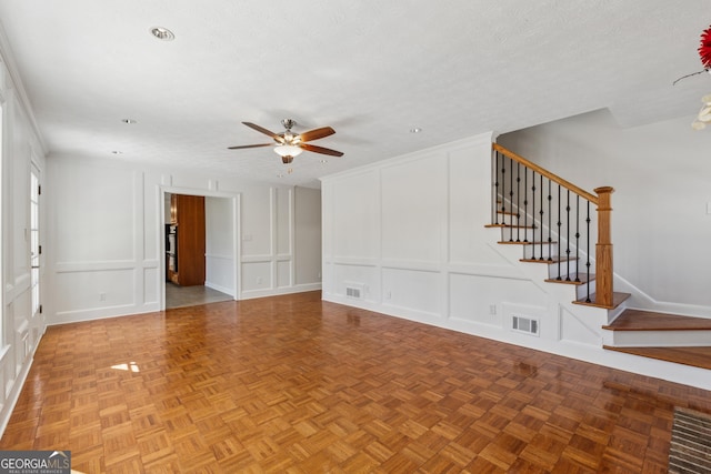 unfurnished living room with visible vents, a ceiling fan, stairs, a textured ceiling, and a decorative wall