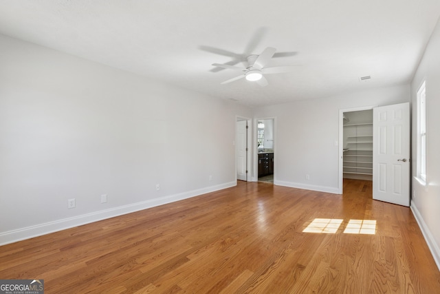 unfurnished bedroom featuring a spacious closet, light wood finished floors, a closet, and baseboards