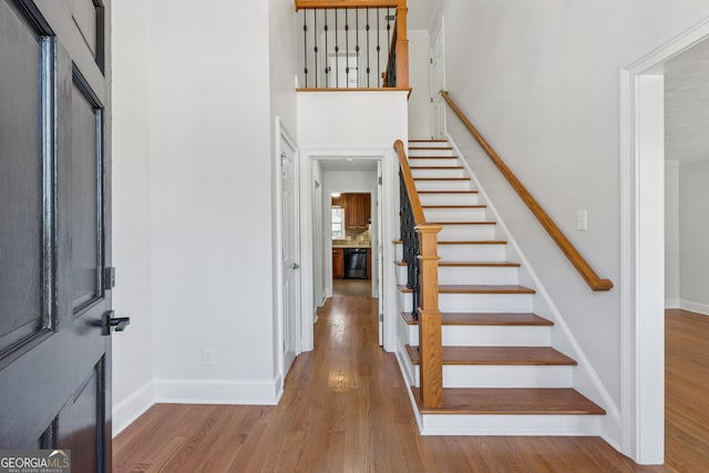 stairs with a towering ceiling, baseboards, and wood finished floors