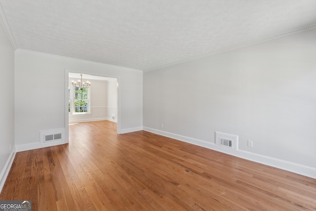 spare room with baseboards, wood finished floors, visible vents, and a notable chandelier