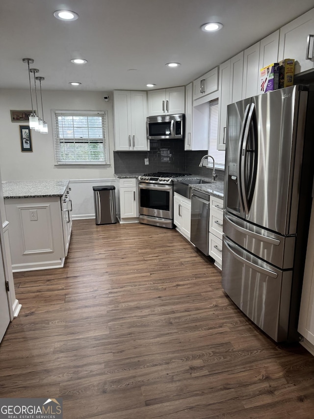 kitchen featuring light stone counters, stainless steel appliances, white cabinetry, backsplash, and dark wood finished floors