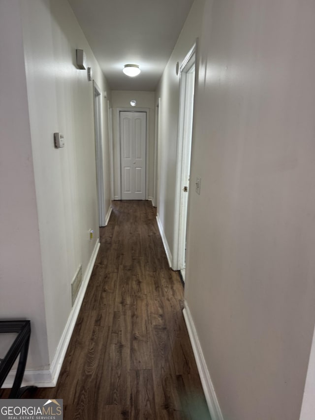 hallway featuring dark wood-style flooring, visible vents, and baseboards