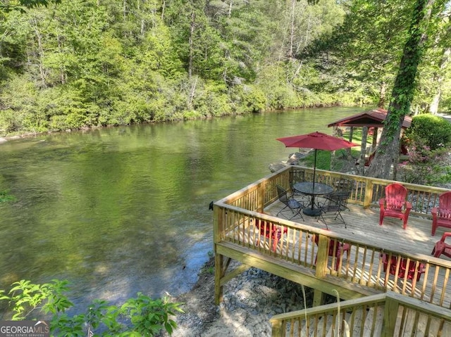 view of dock featuring outdoor dining area, a water view, and a wooded view