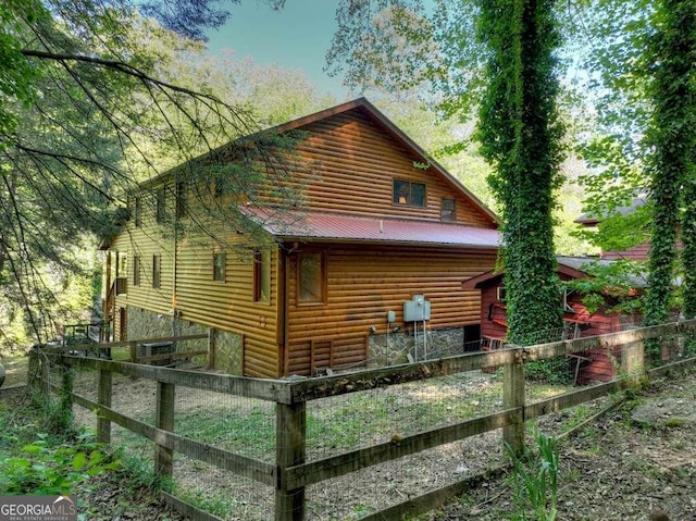 view of home's exterior featuring metal roof, log veneer siding, and fence