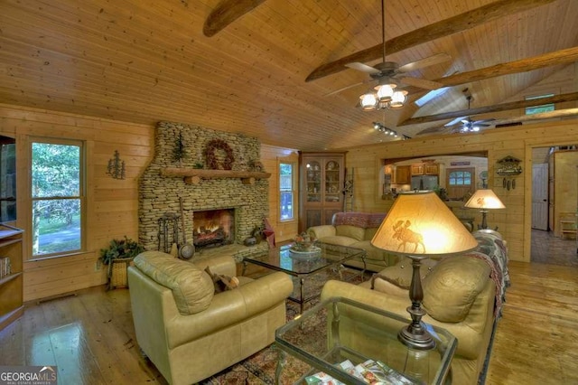 living area featuring vaulted ceiling with beams, light wood finished floors, wood ceiling, wooden walls, and a stone fireplace