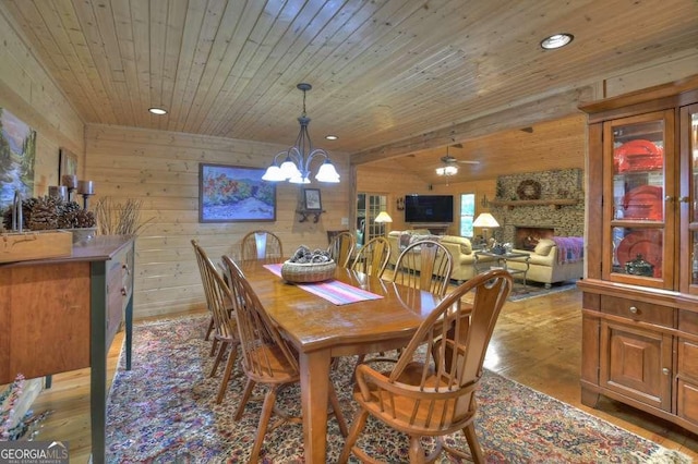 dining space featuring wooden ceiling, wood walls, a stone fireplace, and wood finished floors