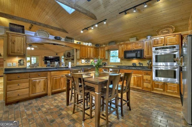 kitchen featuring vaulted ceiling with skylight, brick floor, stainless steel appliances, wood ceiling, and dark countertops