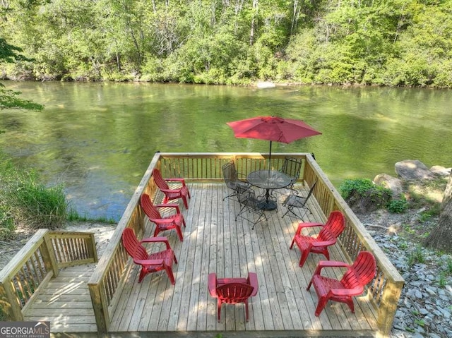 wooden terrace with a water view, a view of trees, and outdoor dining space