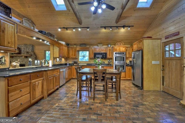 kitchen featuring dark countertops, lofted ceiling with skylight, wood ceiling, appliances with stainless steel finishes, and brick floor