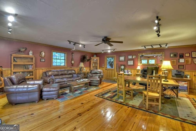 living room with a ceiling fan, a wainscoted wall, crown molding, and hardwood / wood-style flooring