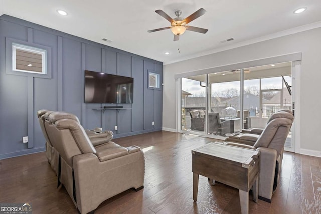 living room with ceiling fan, a decorative wall, dark wood-style flooring, visible vents, and ornamental molding