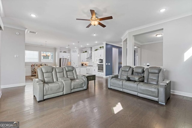 living area featuring baseboards, visible vents, dark wood-style floors, ornamental molding, and ceiling fan with notable chandelier