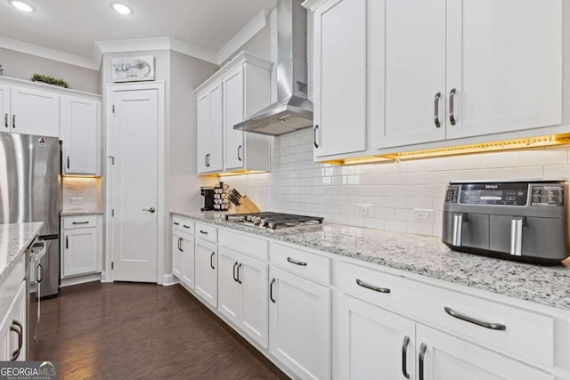 kitchen with ornamental molding, wall chimney exhaust hood, appliances with stainless steel finishes, and white cabinets