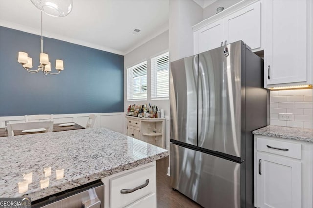 kitchen with ornamental molding, freestanding refrigerator, light stone countertops, white cabinetry, and backsplash