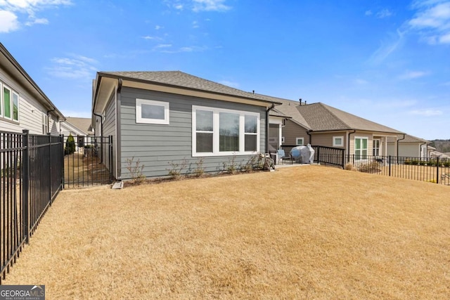 back of house featuring a fenced backyard, a yard, and roof with shingles