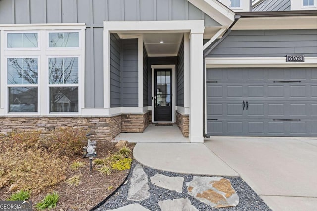 property entrance featuring board and batten siding, stone siding, driveway, and a garage