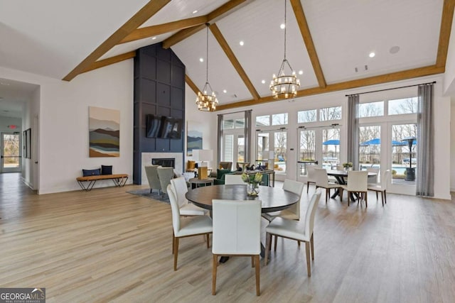 dining room with a chandelier, high vaulted ceiling, a fireplace, light wood finished floors, and beamed ceiling