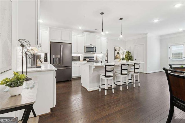 kitchen featuring dark wood finished floors, stainless steel appliances, ornamental molding, white cabinets, and a kitchen breakfast bar