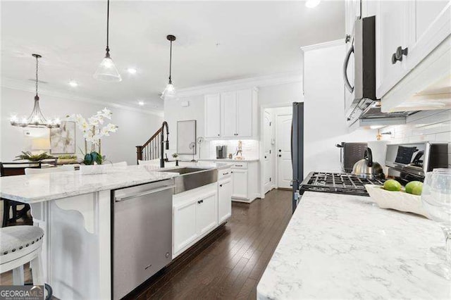 kitchen featuring crown molding, tasteful backsplash, appliances with stainless steel finishes, white cabinetry, and an island with sink