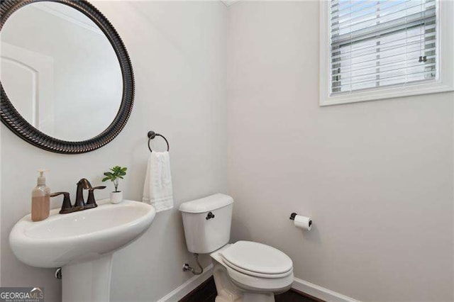 half bathroom with toilet, baseboards, and a sink