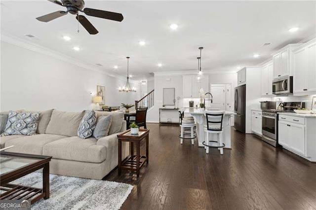 living area with stairs, dark wood-style floors, recessed lighting, ornamental molding, and ceiling fan with notable chandelier