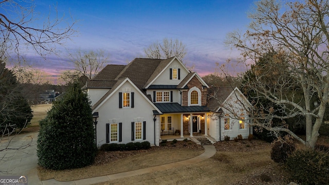 traditional home with stucco siding, a porch, a shingled roof, a standing seam roof, and metal roof