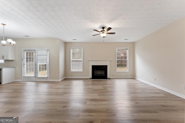 unfurnished living room with a fireplace with raised hearth, plenty of natural light, light wood-style flooring, and ceiling fan with notable chandelier