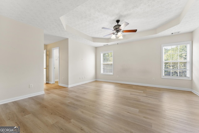 spare room featuring plenty of natural light, light wood-style floors, visible vents, and a tray ceiling