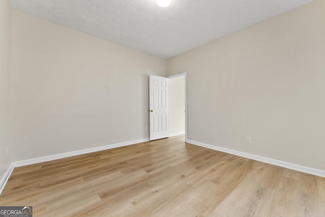 unfurnished room featuring a textured ceiling, light wood finished floors, and baseboards