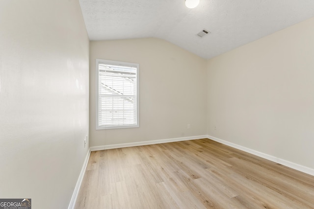 empty room featuring a textured ceiling, visible vents, baseboards, vaulted ceiling, and light wood-style floors