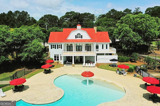 rear view of house featuring a patio, a balcony, fence, a fenced in pool, and a chimney