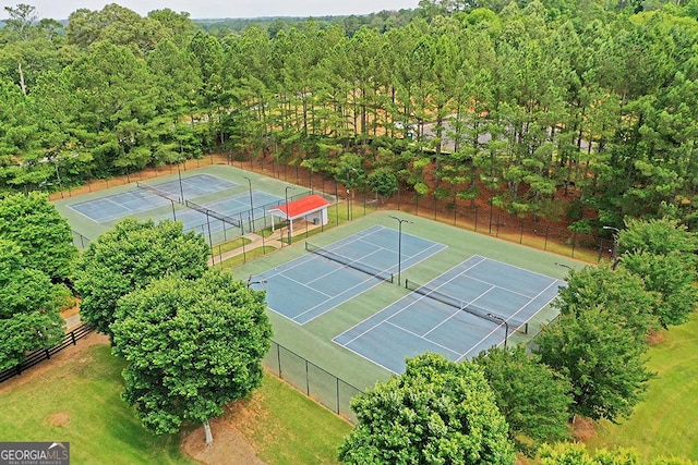 view of tennis court featuring fence and a wooded view