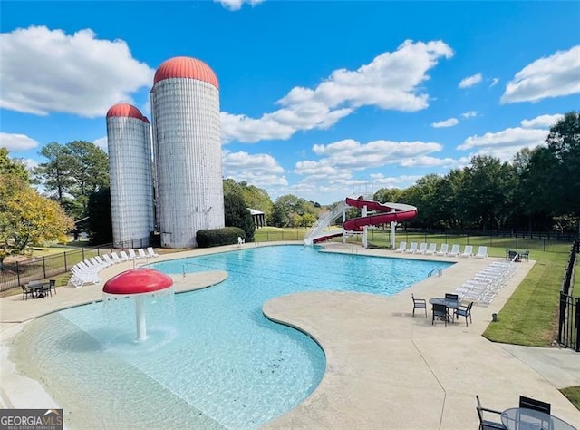 pool with a yard, a water slide, a patio area, and fence