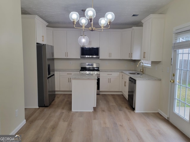 kitchen featuring light stone counters, stainless steel appliances, a kitchen island, a sink, and white cabinetry