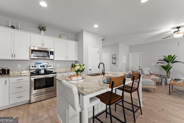 kitchen with appliances with stainless steel finishes, light wood-style floors, white cabinetry, and a sink