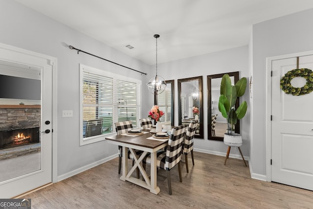 dining room featuring a stone fireplace, wood finished floors, visible vents, baseboards, and an inviting chandelier