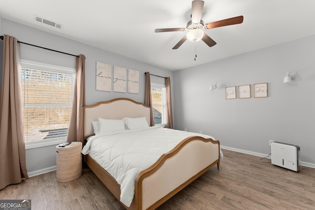 bedroom featuring a ceiling fan, wood finished floors, visible vents, and baseboards