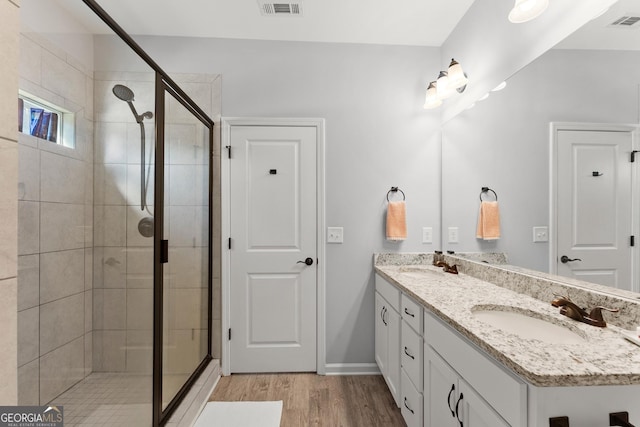 full bath featuring double vanity, wood finished floors, a stall shower, and a sink