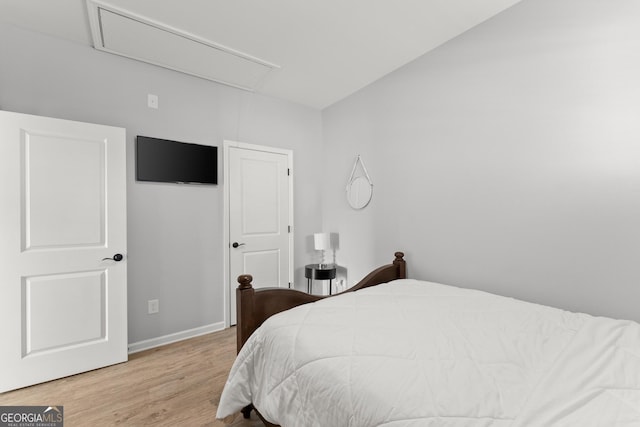 bedroom featuring attic access, baseboards, and wood finished floors