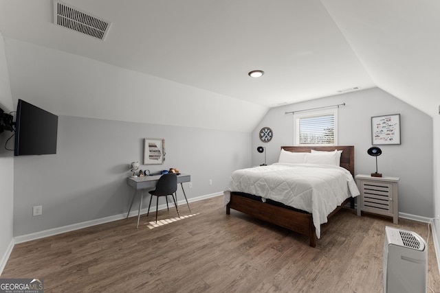 bedroom with vaulted ceiling, wood finished floors, visible vents, and baseboards