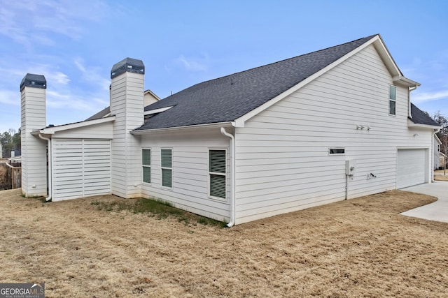 back of property featuring a garage, a chimney, and roof with shingles