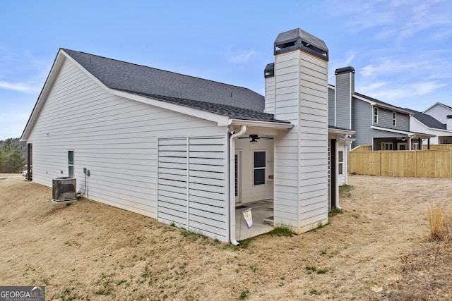 rear view of house with central AC, roof with shingles, and fence