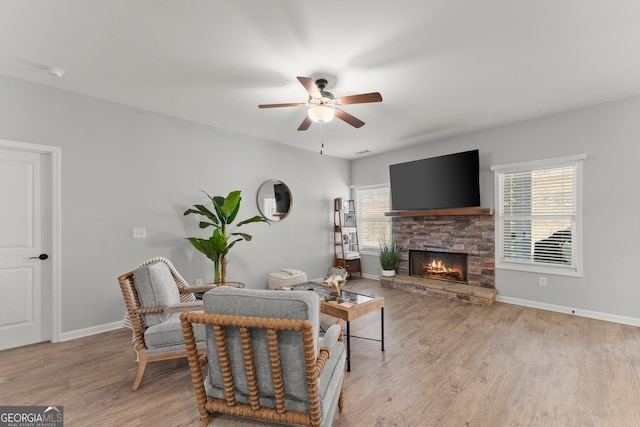 living area featuring light wood-style floors, a fireplace, baseboards, and a ceiling fan