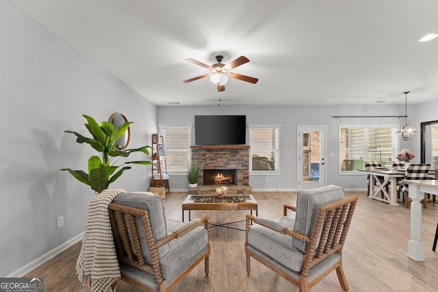 living room featuring light wood-style flooring, baseboards, a ceiling fan, and a stone fireplace