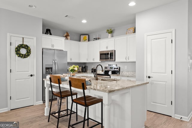 kitchen featuring white cabinets, appliances with stainless steel finishes, light stone counters, light wood-style floors, and a sink