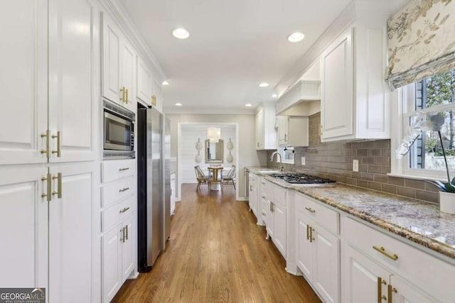 kitchen with a sink, decorative backsplash, white cabinets, light wood-style floors, and appliances with stainless steel finishes