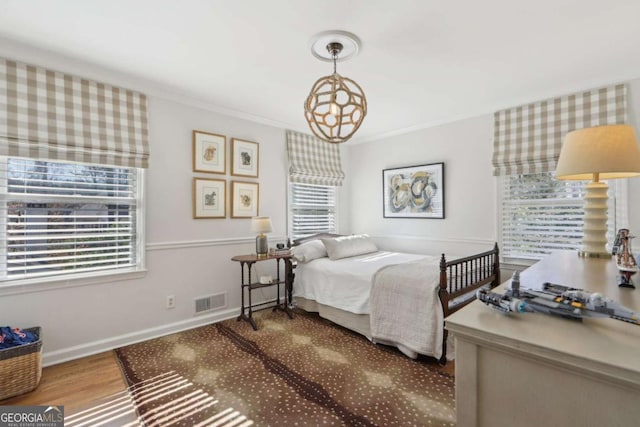 bedroom featuring baseboards, wood finished floors, visible vents, and ornamental molding