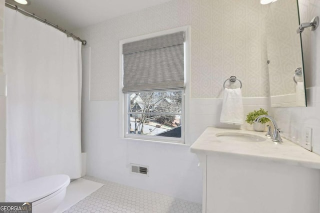 full bath featuring visible vents, toilet, vanity, wainscoting, and tile walls