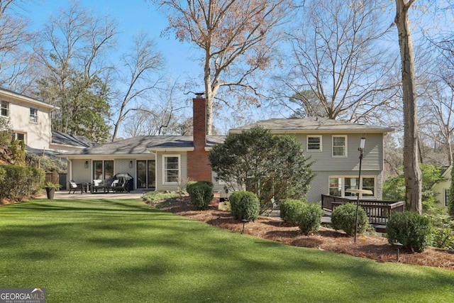 rear view of property featuring a wooden deck, a yard, a chimney, a patio area, and brick siding